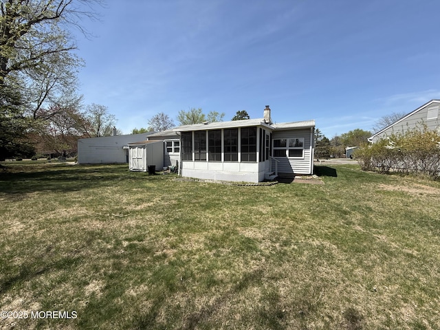 rear view of house featuring a chimney, a sunroom, and a lawn