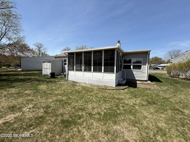 rear view of property with a storage shed, a chimney, a sunroom, and a yard