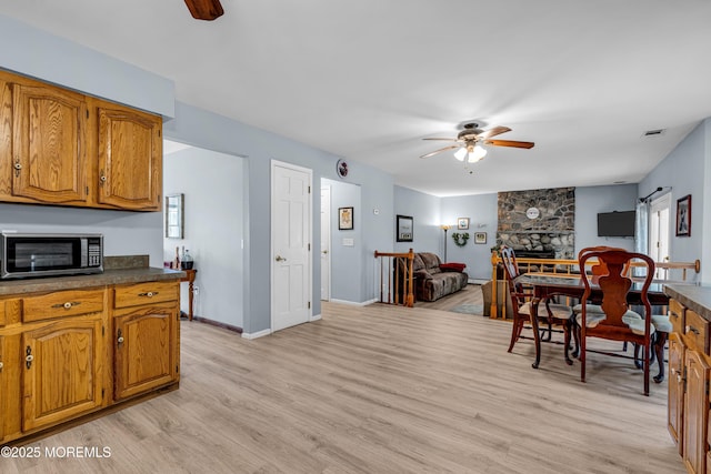 kitchen with dark countertops, stainless steel microwave, brown cabinetry, open floor plan, and ceiling fan