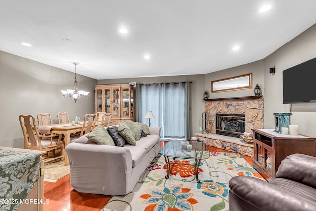 living area with a stone fireplace, an inviting chandelier, light wood-style flooring, and recessed lighting