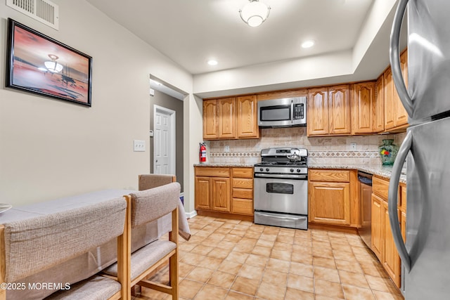 kitchen featuring appliances with stainless steel finishes, brown cabinetry, visible vents, and tasteful backsplash