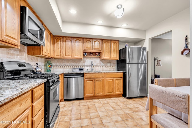 kitchen with light stone countertops, appliances with stainless steel finishes, decorative backsplash, and a sink