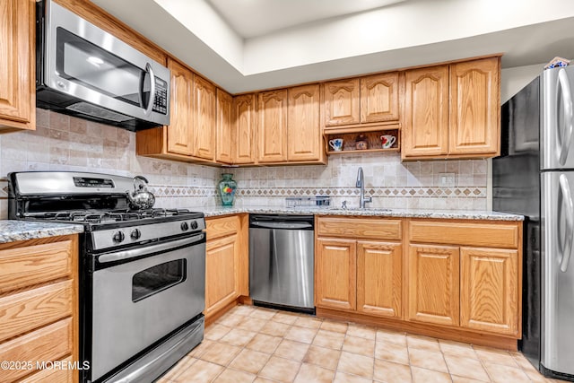 kitchen with tasteful backsplash, appliances with stainless steel finishes, a sink, and light stone countertops