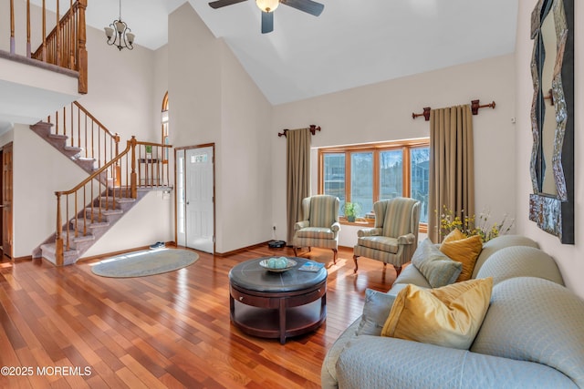 living room with stairs, hardwood / wood-style floors, ceiling fan with notable chandelier, and a towering ceiling