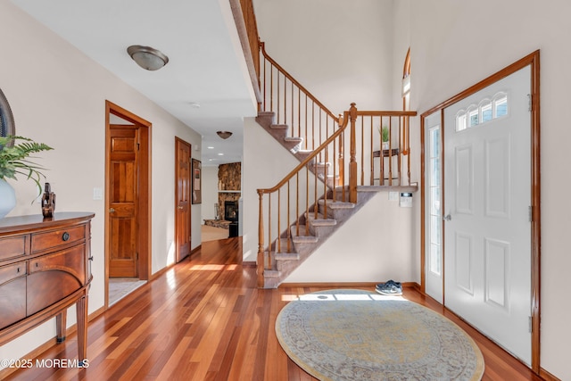 entrance foyer with stairs, a stone fireplace, baseboards, and light wood-style floors