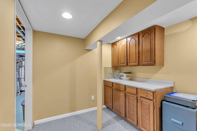 kitchen with baseboards, brown cabinetry, light colored carpet, light countertops, and recessed lighting