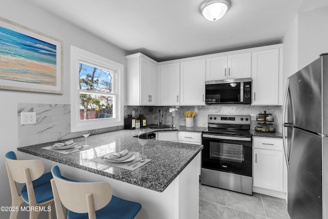 kitchen with appliances with stainless steel finishes, a breakfast bar, white cabinets, and a peninsula