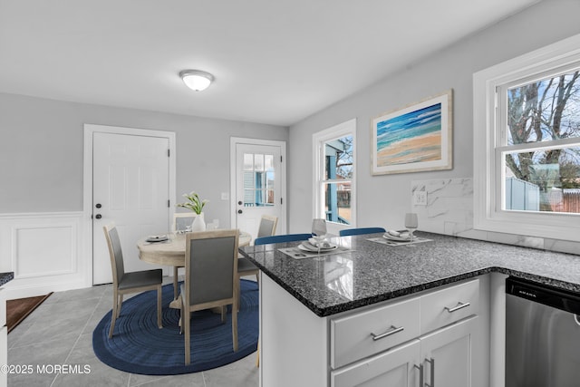 kitchen with dishwasher, wainscoting, dark stone countertops, white cabinetry, and light tile patterned flooring