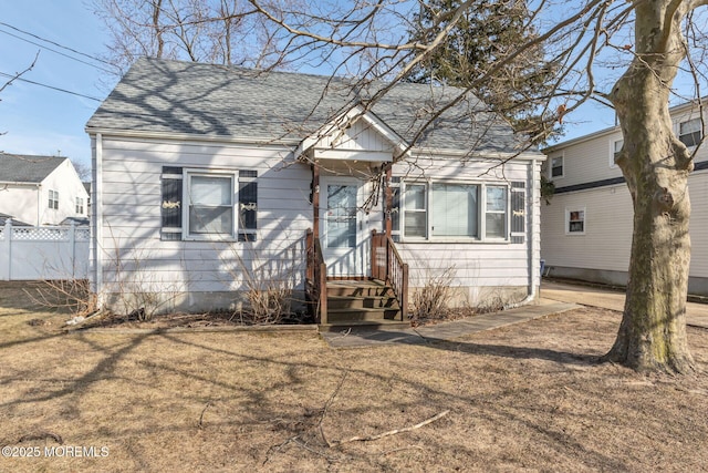 view of front facade featuring a shingled roof, a front yard, and fence