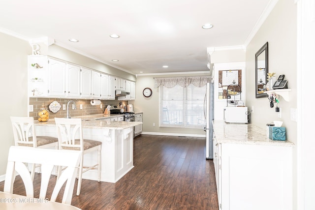 kitchen with a breakfast bar area, stainless steel appliances, white cabinetry, a peninsula, and under cabinet range hood