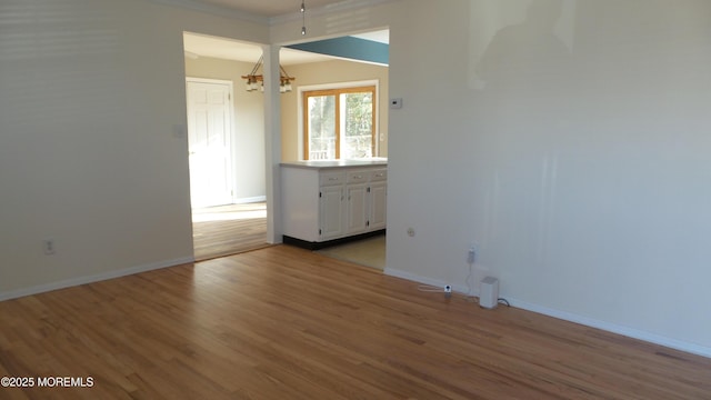 unfurnished room with a notable chandelier, light wood-style flooring, and baseboards