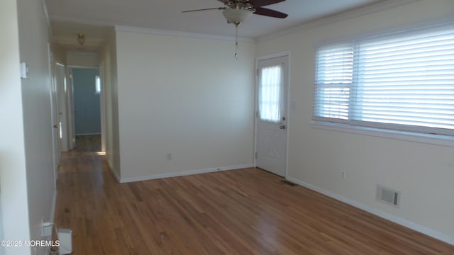 spare room with baseboards, visible vents, a ceiling fan, ornamental molding, and dark wood-style flooring