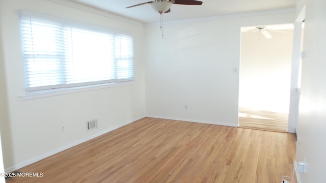 spare room with a ceiling fan, baseboards, light wood-style floors, visible vents, and crown molding