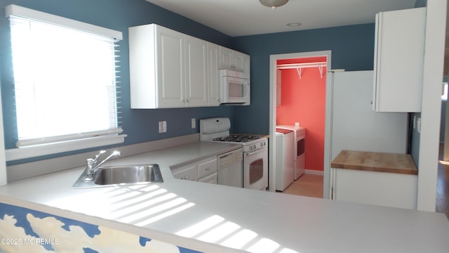 kitchen featuring white appliances, independent washer and dryer, a peninsula, white cabinetry, and a sink