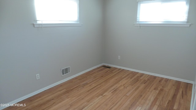 spare room featuring light wood-style floors, baseboards, visible vents, and a wealth of natural light