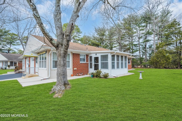 rear view of house with brick siding, a yard, an attached garage, a sunroom, and driveway