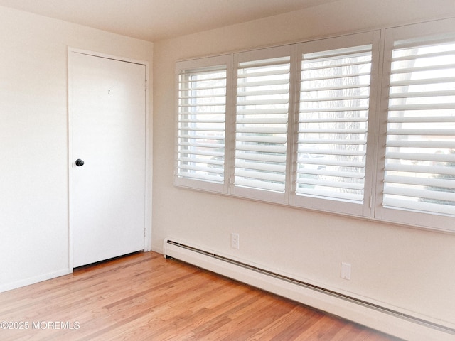 unfurnished room featuring a baseboard heating unit and light wood-type flooring