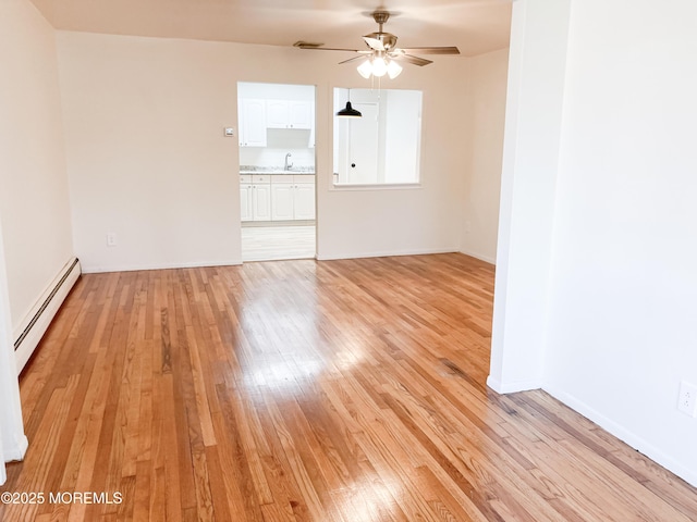 unfurnished room with baseboards, a ceiling fan, a baseboard radiator, light wood-style floors, and a sink