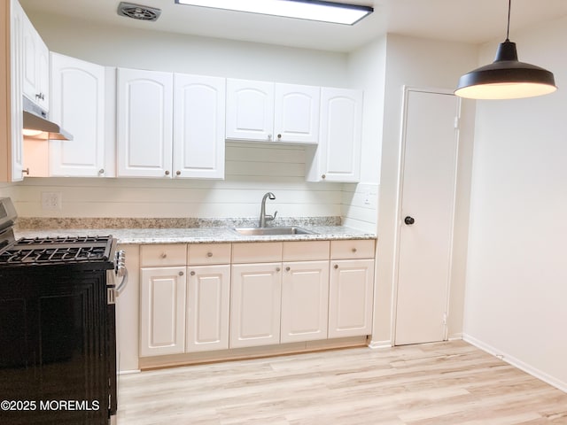 kitchen featuring light wood finished floors, stainless steel gas range oven, visible vents, under cabinet range hood, and a sink