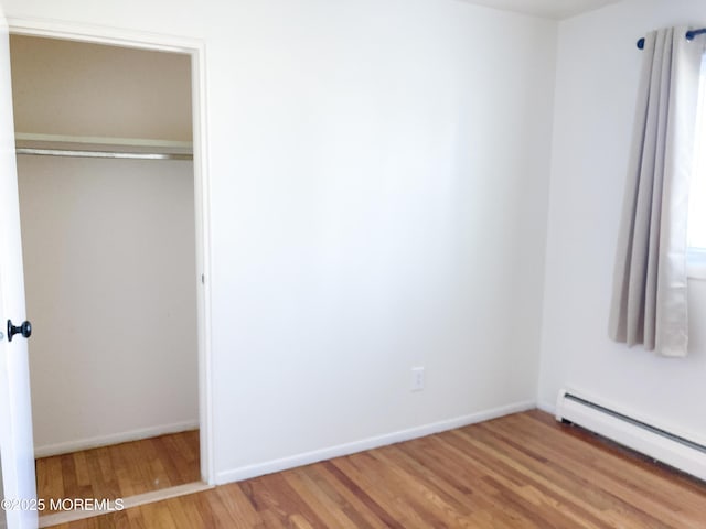 unfurnished bedroom featuring a closet, baseboards, baseboard heating, and wood finished floors