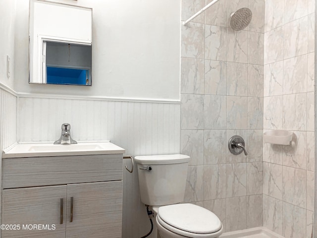 full bath featuring a wainscoted wall, vanity, toilet, and tiled shower