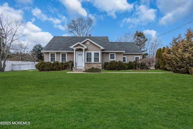 view of front of house featuring stone siding, a shingled roof, fence, and a front yard