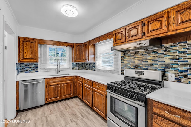 kitchen with brown cabinets, light countertops, appliances with stainless steel finishes, a sink, and under cabinet range hood