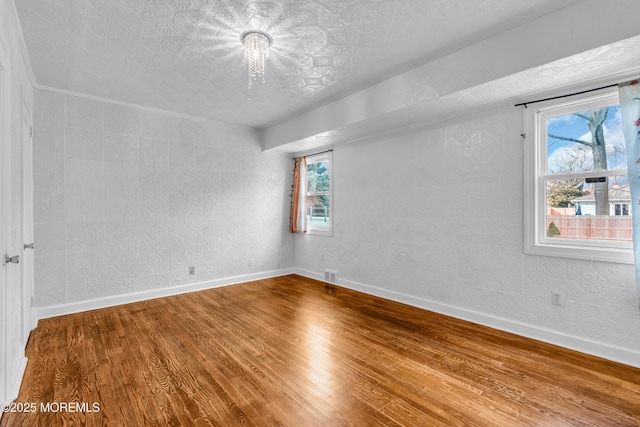 empty room with a textured ceiling, wood finished floors, visible vents, and baseboards