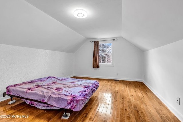 bedroom with vaulted ceiling, wood-type flooring, and baseboards