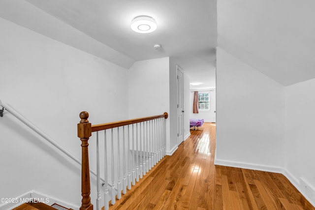 hall with lofted ceiling, hardwood / wood-style flooring, baseboards, and an upstairs landing