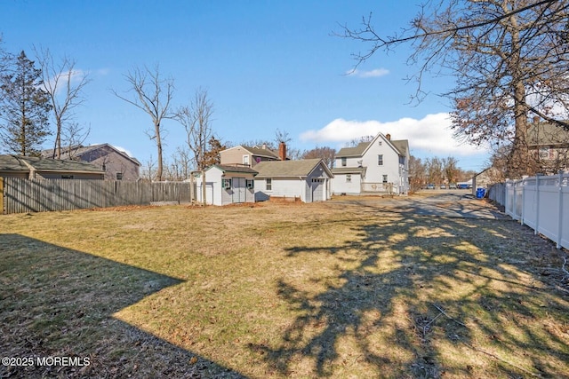 view of yard with a fenced backyard, a residential view, a shed, and an outbuilding