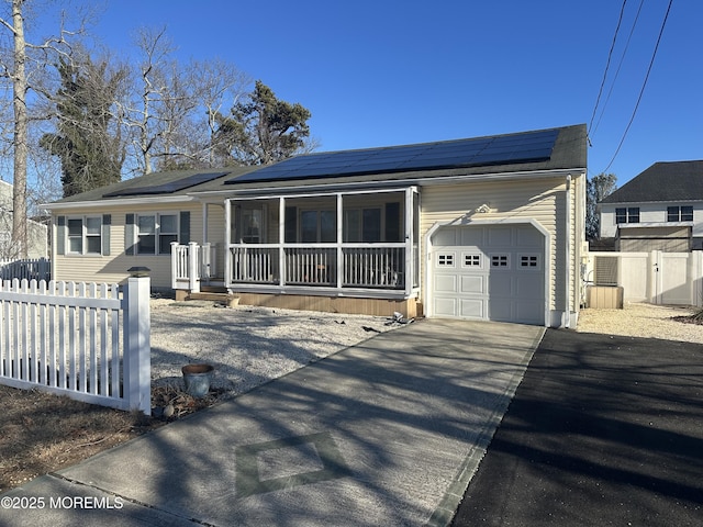 ranch-style home featuring driveway, an attached garage, fence, and roof mounted solar panels