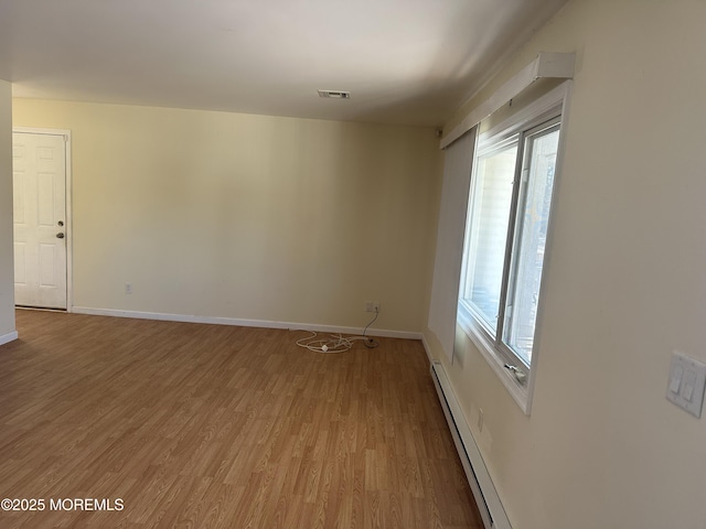 spare room with baseboard heating, wood finished floors, visible vents, and baseboards