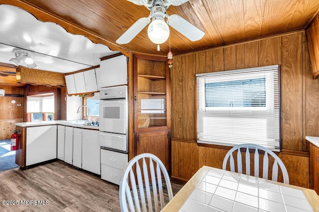 kitchen with white oven, a sink, wooden walls, wood finished floors, and wooden ceiling