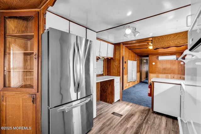 kitchen with light countertops, light wood-style floors, freestanding refrigerator, white cabinets, and wooden walls