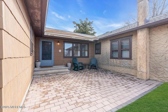 view of exterior entry featuring a patio area, a chimney, and roof with shingles