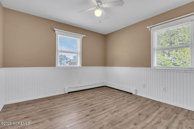 empty room featuring a baseboard heating unit, wood finished floors, a wainscoted wall, and ceiling fan