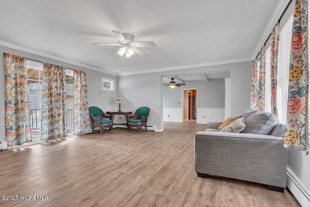 sitting room featuring light wood finished floors, baseboard heating, ornamental molding, and a wainscoted wall