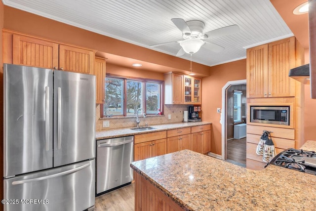 kitchen with tasteful backsplash, light stone countertops, ornamental molding, appliances with stainless steel finishes, and a sink