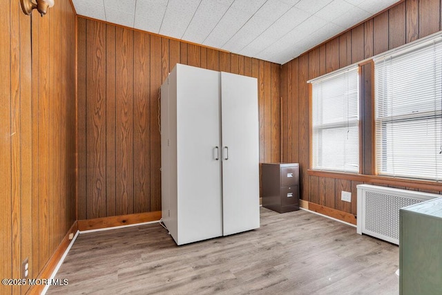 interior space with light wood finished floors, wood walls, radiator, and a closet