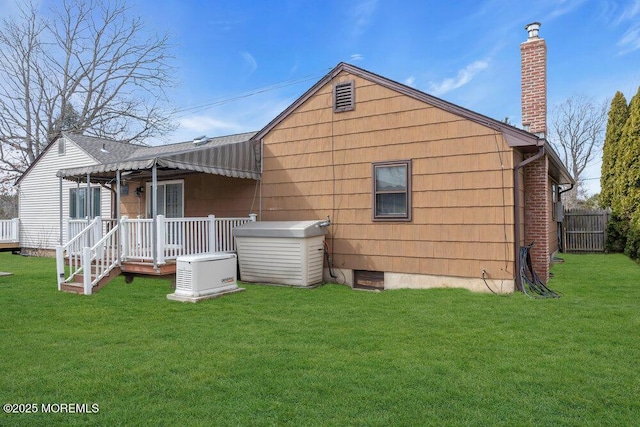 rear view of house with a chimney, a yard, and fence