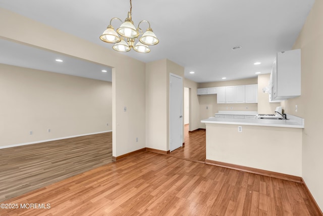 kitchen featuring light wood finished floors, baseboards, open floor plan, light countertops, and white cabinets