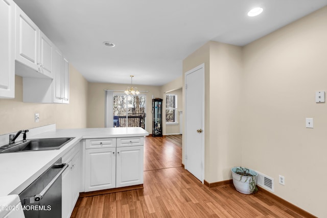 kitchen featuring a sink, light wood-style floors, a peninsula, white cabinets, and dishwasher