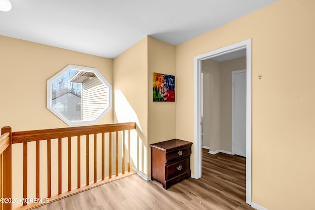 corridor with an upstairs landing, baseboards, and wood finished floors