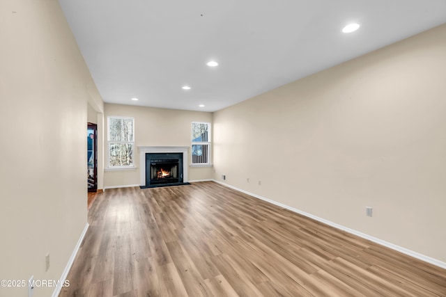 unfurnished living room featuring recessed lighting, baseboards, a fireplace with flush hearth, and light wood-style flooring