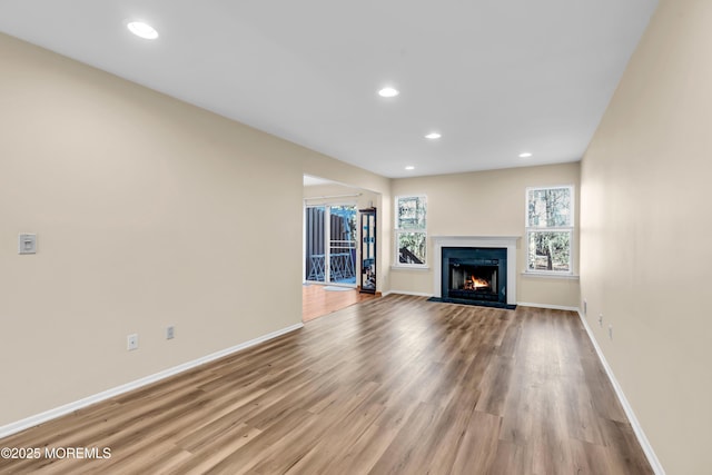 unfurnished living room with a fireplace with flush hearth, recessed lighting, baseboards, and wood finished floors