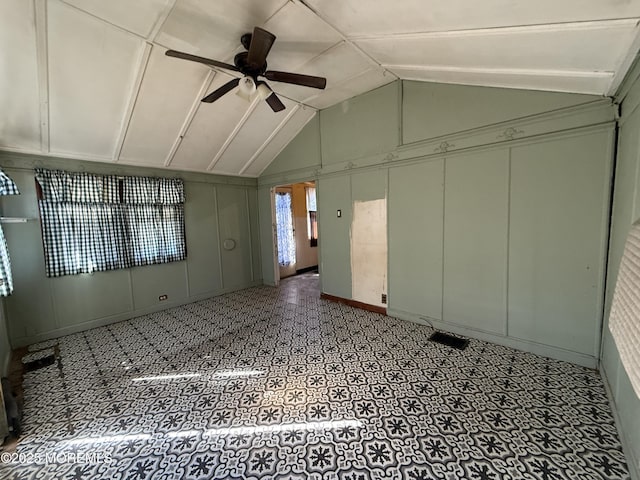 empty room featuring light floors, vaulted ceiling, a ceiling fan, and a decorative wall