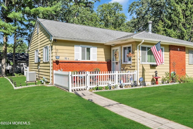 view of front facade with brick siding, a shingled roof, central AC unit, a front yard, and fence