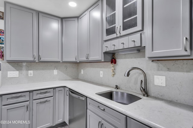 kitchen with glass insert cabinets, gray cabinetry, a sink, and stainless steel dishwasher