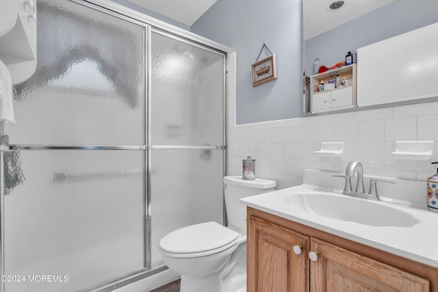 bathroom with a stall shower, vanity, toilet, and tile walls